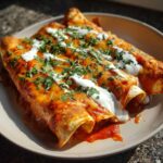 Three baked cheese enchiladas covered in red sauce, melted cheddar, sour cream, and fresh cilantro.