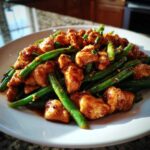 A close-up of saucy chicken pieces mixed with bright green beans, representing a perfect chicken and green beans dinner.