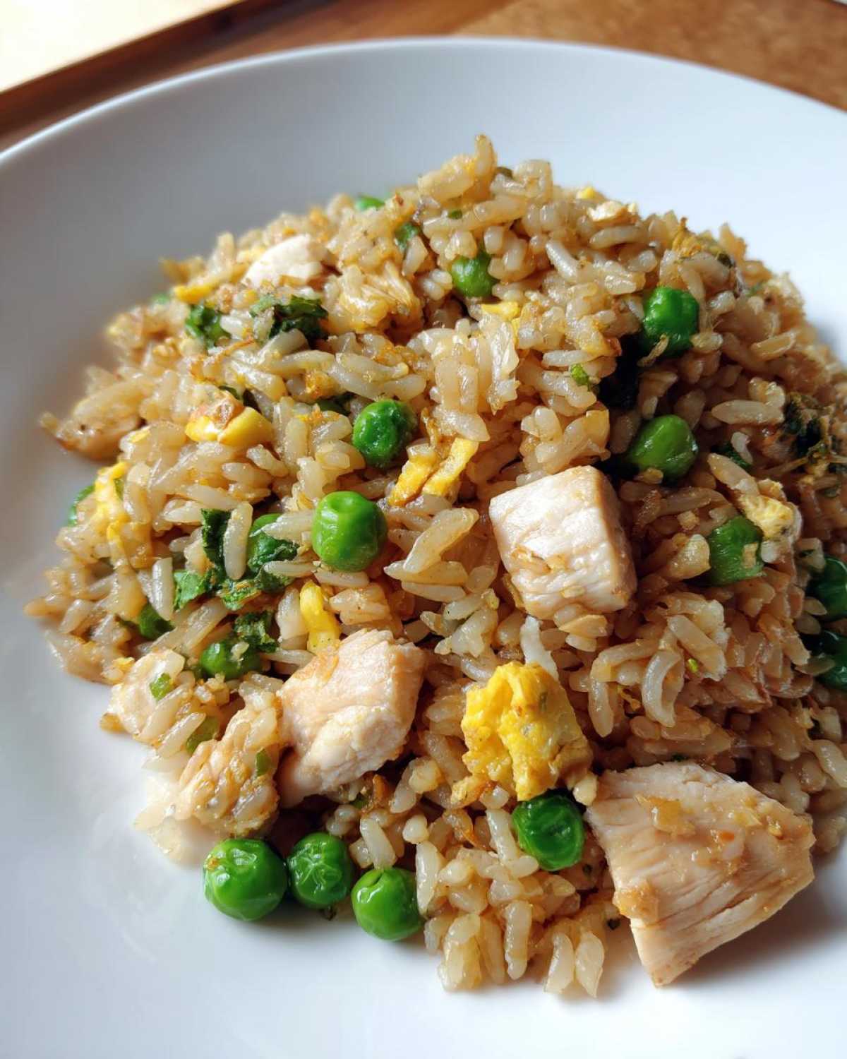 A close-up serving of homemade chicken fried rice featuring chunks of white chicken meat, bright green peas, and scrambled egg.