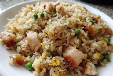 A close-up shot of a serving of flavorful chicken fried rice with visible pieces of chicken, scrambled egg, and green peas.