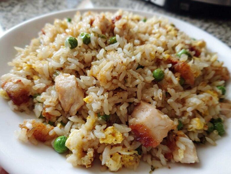 A close-up shot of a serving of flavorful chicken fried rice with visible pieces of chicken, scrambled egg, and green peas.