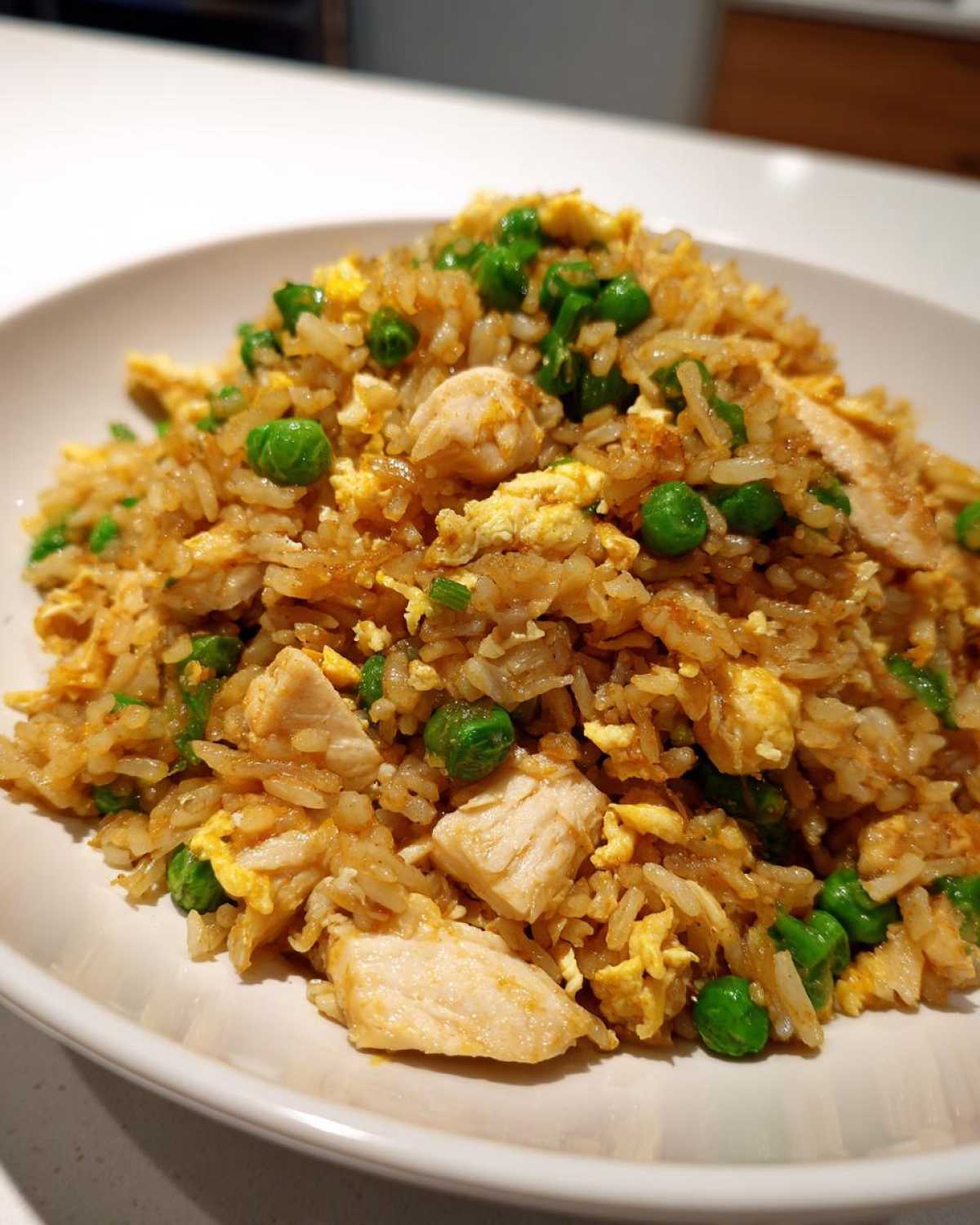 Close-up of a hearty serving of homemade chicken fried rice featuring chunks of chicken, scrambled egg, and bright green peas.