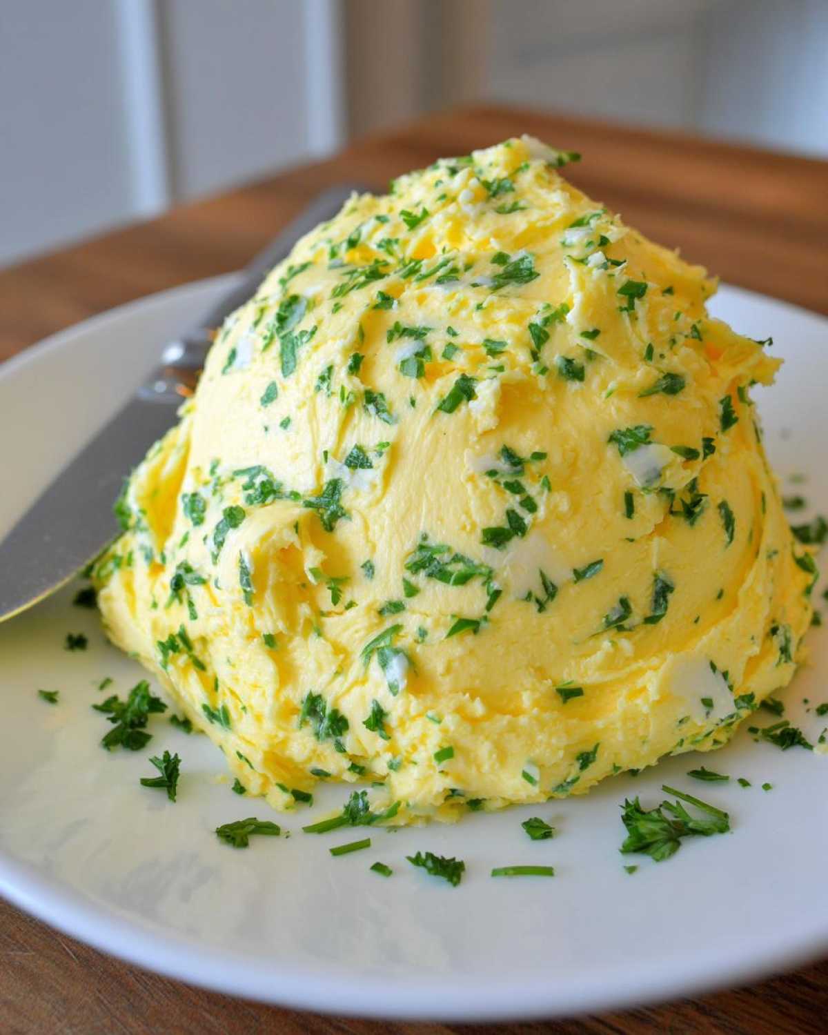 A mound of freshly whipped garlic butter mixed with chopped green herbs, likely parsley, served on a white plate.