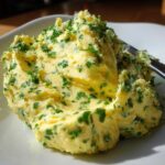 A mound of homemade garlic butter mixed with bright green chopped parsley served on a white dish.