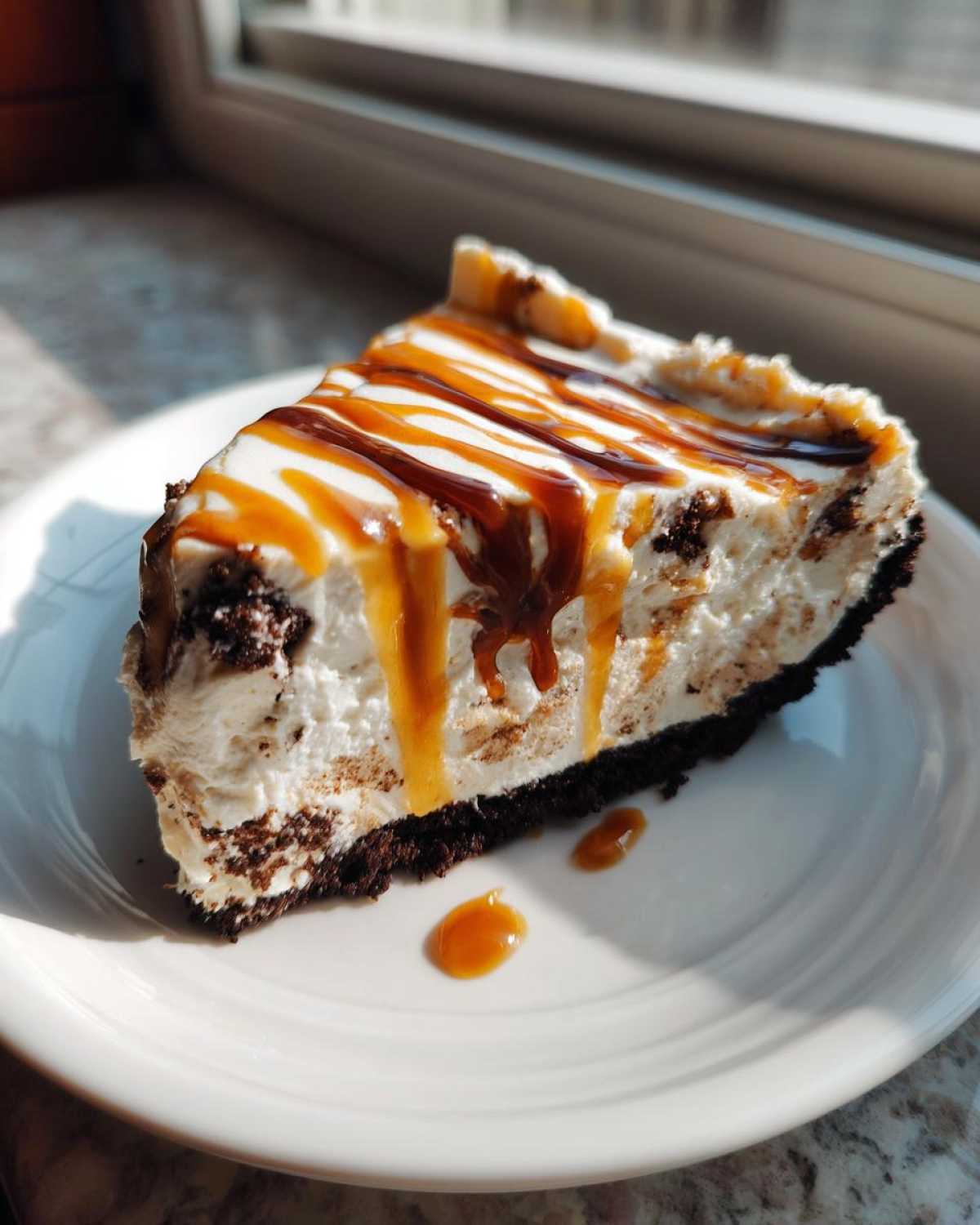 A decadent slice of no-bake ice cream pie with a dark crust, creamy filling, and caramel drizzle.