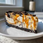 A decadent slice of no-bake ice cream pie featuring a dark cookie crust, creamy filling, caramel drizzle, and cookie crumbles.