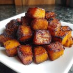 A pile of perfectly caramelized and slightly charred roasted butternut squash cubes on a white plate.