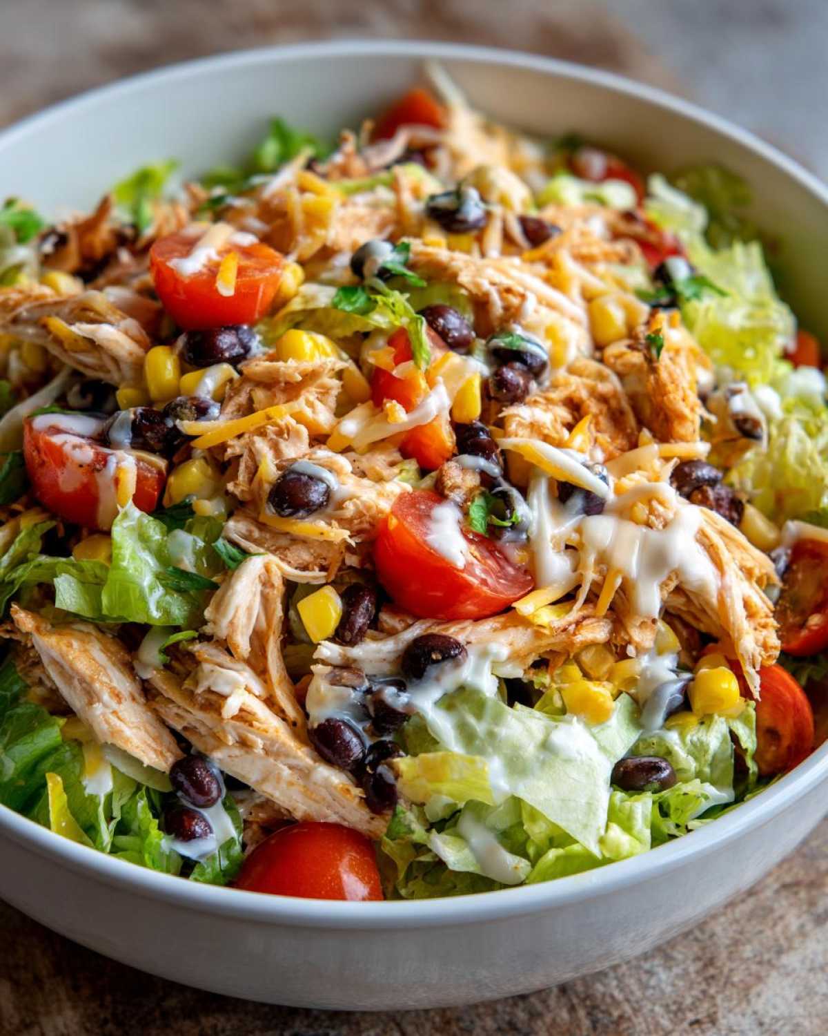 Close-up of a vibrant southwest salad featuring shredded chicken, black beans, corn, tomatoes, cheese, and creamy dressing.