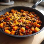 Close-up of a savory sweet potato skillet dinner with ground meat, black beans, peppers, and melted cheddar cheese.