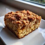 A square slice of apple baked oatmeal topped with a thick cinnamon streusel topping, served on a white plate.