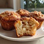 Four Apple Cinnamon Greek Yogurt Muffins on a white plate, one cut open showing the moist interior.
