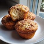 A stack of four Apple Cinnamon Greek Yogurt Muffins, one broken open showing the moist interior and cinnamon sugar topping.