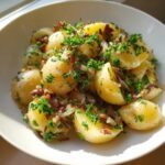 Close-up of warm Authentic German Potato Salad featuring boiled potatoes tossed with bacon bits, onions, and fresh parsley.