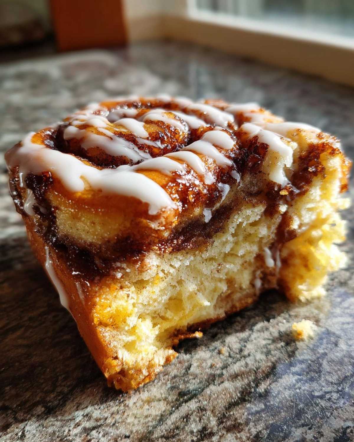 Close-up of a soft, gooey Banana Bread Batter Cinnamon Buns swirl topped with white icing drizzle.