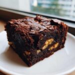 A close-up of a fudgy, dark chocolate Banana Bread Brownies with Walnuts for Snack Time on a white plate.