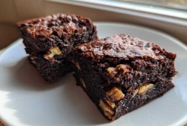 Two rich, fudgy Banana Bread Brownies with Walnuts stacked on a white plate near a window.