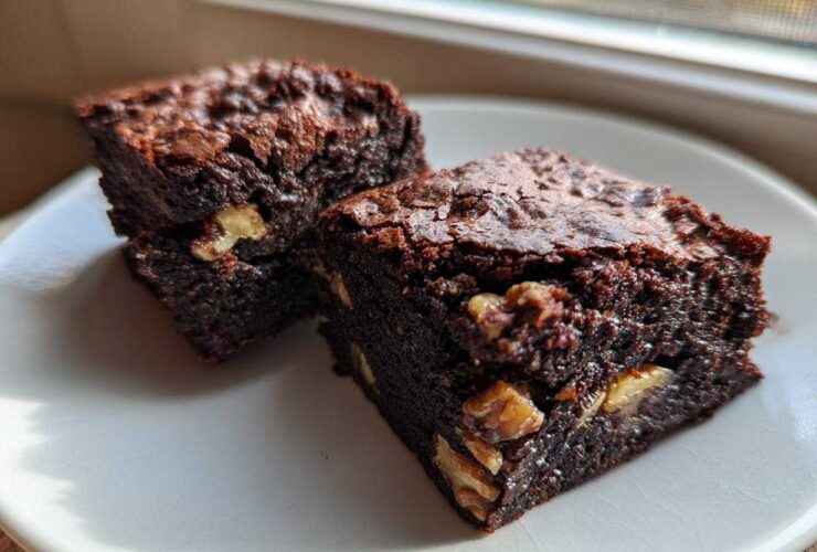 Two rich, fudgy Banana Bread Brownies with Walnuts stacked on a white plate near a window.