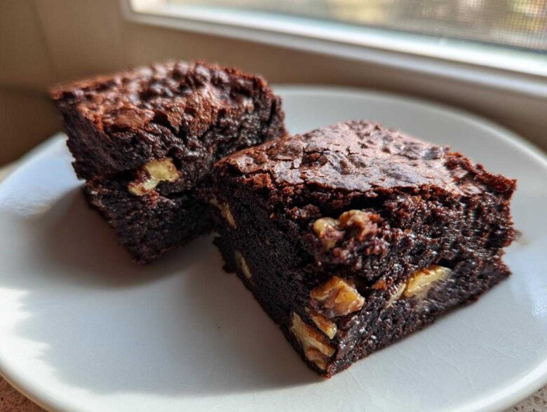 Two rich, fudgy Banana Bread Brownies with Walnuts stacked on a white plate near a window.