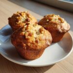Three golden-brown Banana Walnut Cottage Cheese Muffin Breakfast items topped with walnuts, sitting on a white plate.