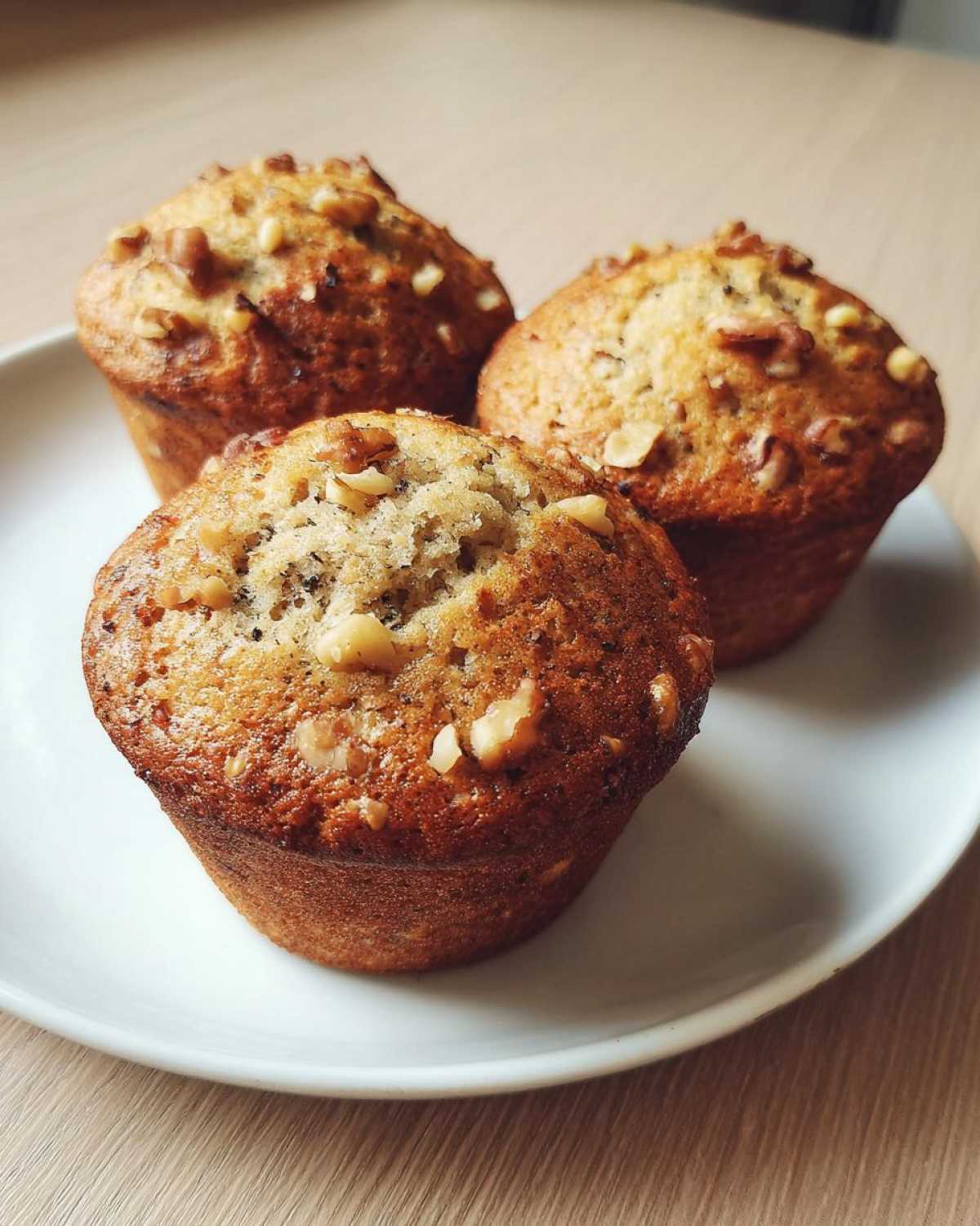 Three freshly baked Banana Walnut Cottage Cheese Muffin Breakfast items displayed on a white plate.