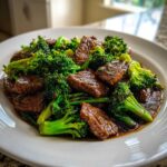 Close-up of tender slices of Beef and Broccoli Stir Fry coated in a rich brown sauce on a white plate.