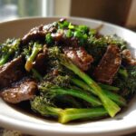 A close-up of tender slices of beef coated in dark sauce mixed with bright green broccoli florets in a white bowl, featuring the Best Beef and Broccoli Stir Fry.