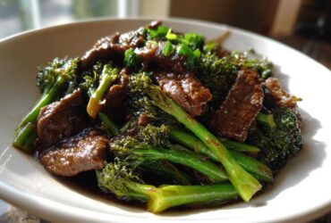 A close-up of tender slices of beef coated in dark sauce mixed with bright green broccoli florets in a white bowl, featuring the Best Beef and Broccoli Stir Fry.