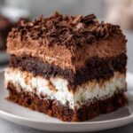 A rich, layered slice of brownie refrigerator cake featuring dark chocolate cake, white cream, and chocolate mousse topping with shavings.