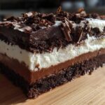 Close-up of a decadent slice of brownie refrigerator cake showing five distinct layers of chocolate cake, mousse, and cream.