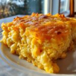 A close-up of a moist slice of cheesy corn casserole with visible kernels of corn and a golden-brown baked cheese crust.