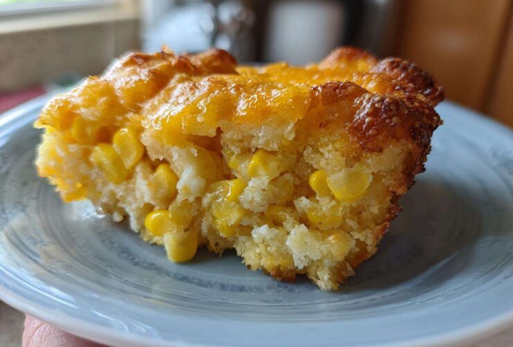 A close-up of a moist slice of cheesy corn casserole showing whole corn kernels baked into the bread.