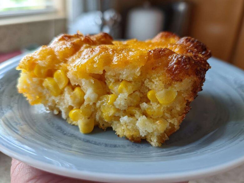 A close-up of a moist slice of cheesy corn casserole showing whole corn kernels baked into the bread.