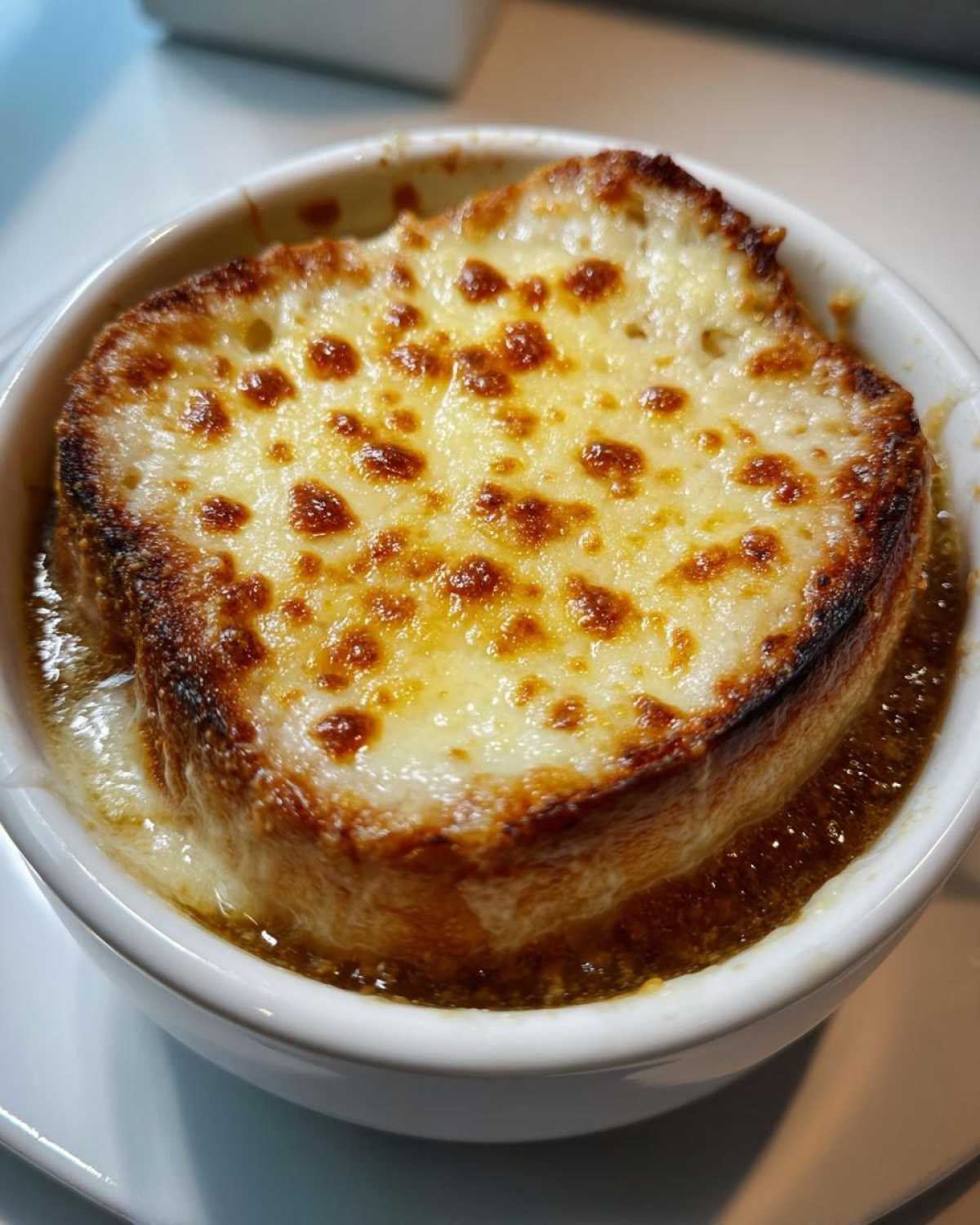 Close-up of a bubbling bowl of french onion soup topped with a thick layer of broiled, melted Gruyère cheese.