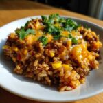A close-up serving of cheesy mexican rice casserole mixed with ground meat and corn, topped with melted cheese and fresh cilantro.