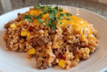 A serving of cheesy mexican rice casserole mixed with ground beef and corn, topped with melted cheddar and cilantro.
