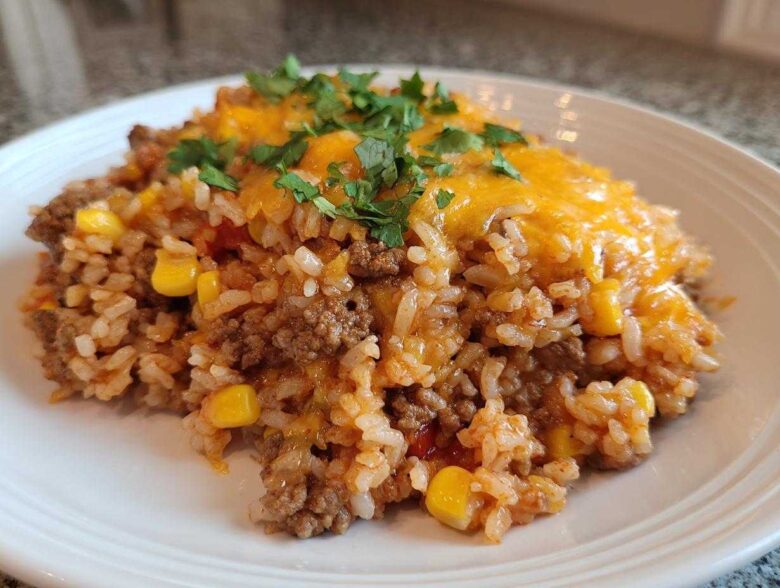 A serving of cheesy mexican rice casserole mixed with ground beef and corn, topped with melted cheddar and cilantro.