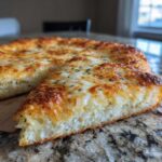 A slice of cheesy, golden-brown keto pizza crust topped with herbs, showing a thick, fluffy interior.