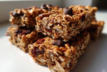 A stack of chewy homemade granola bars featuring oats, dried fruit, and chocolate chips, brightly lit.