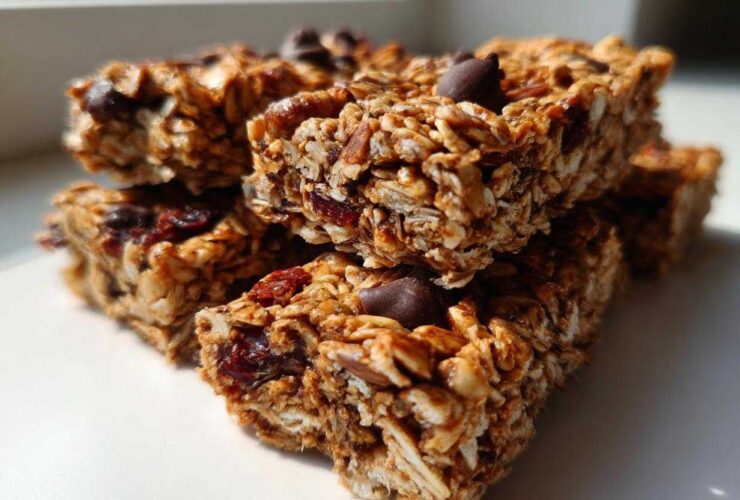A stack of chewy homemade granola bars featuring oats, dried fruit, and chocolate chips, brightly lit.