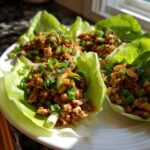 Four fresh chicken lettuce wraps filled with savory ground chicken mixture and topped with green onions.