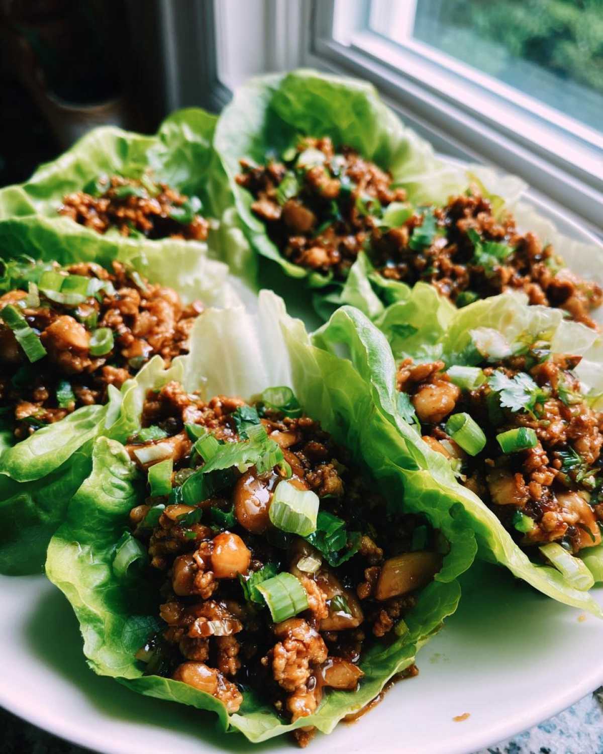 Several servings of delicious chicken lettuce wraps filled with savory ground chicken mixture and topped with fresh green onions.
