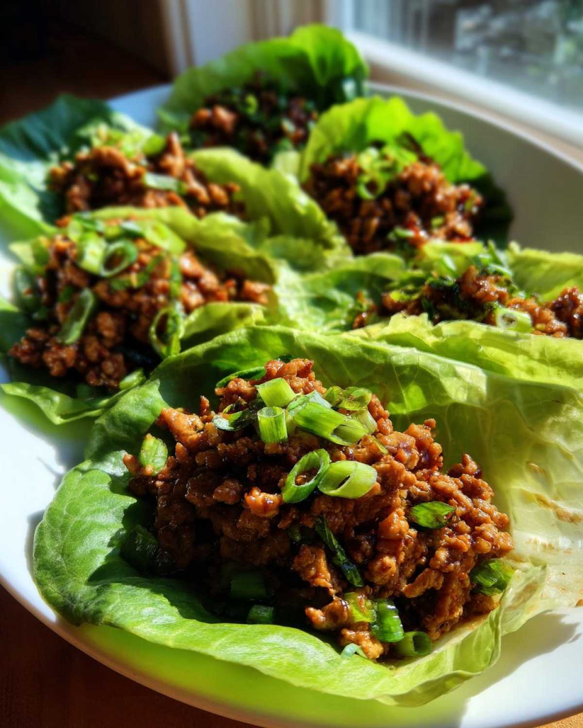 Close-up of several fresh chicken lettuce wraps filled with savory ground chicken mixture and topped with sliced green onions.