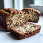 A close-up of a freshly baked chocolate chip vegan banana bread loaf with one slice cut and resting in front.