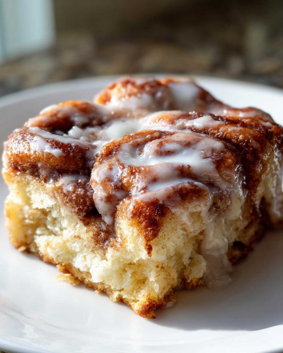 A close-up of a warm, fluffy serving of cinnamon roll casserole topped with thick white icing.