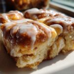 A close-up, sunlit serving of soft Cinnamon roll casserole topped with thick white icing.