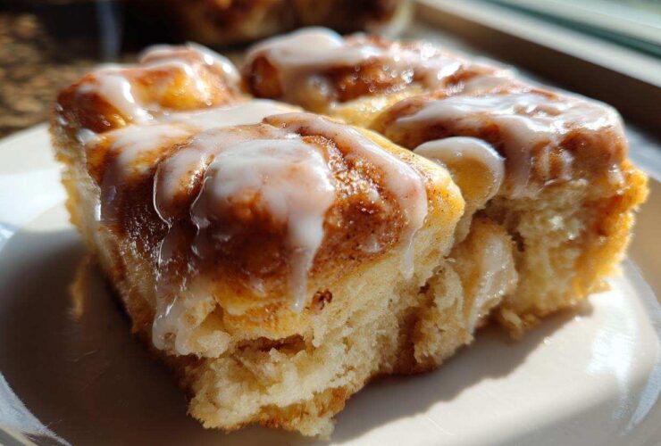 A close-up, sunlit serving of soft Cinnamon roll casserole topped with thick white icing.