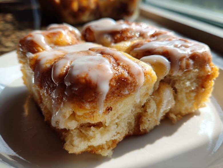 A close-up, sunlit serving of soft Cinnamon roll casserole topped with thick white icing.