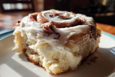 Close-up of a fluffy cinnamon roll generously topped with thick, white cream cheese frosting.