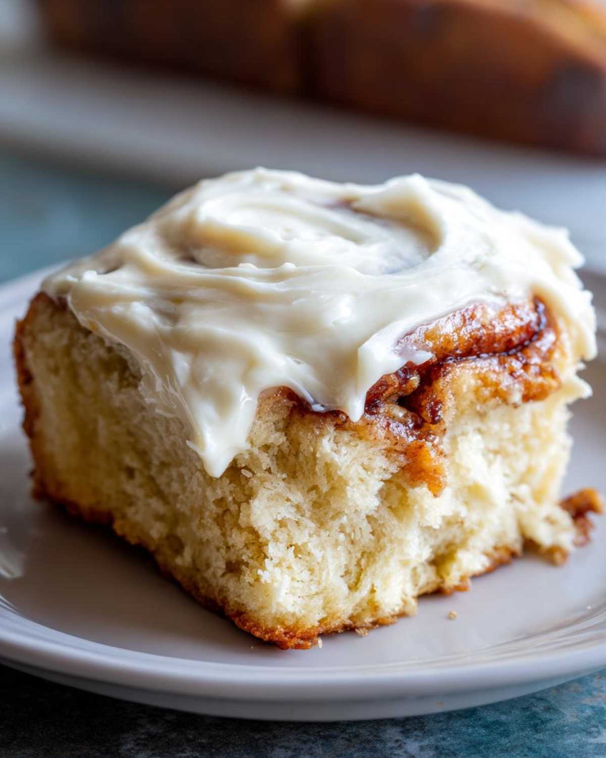 A close-up of a soft cinnamon roll generously topped with thick, white cream cheese frosting.