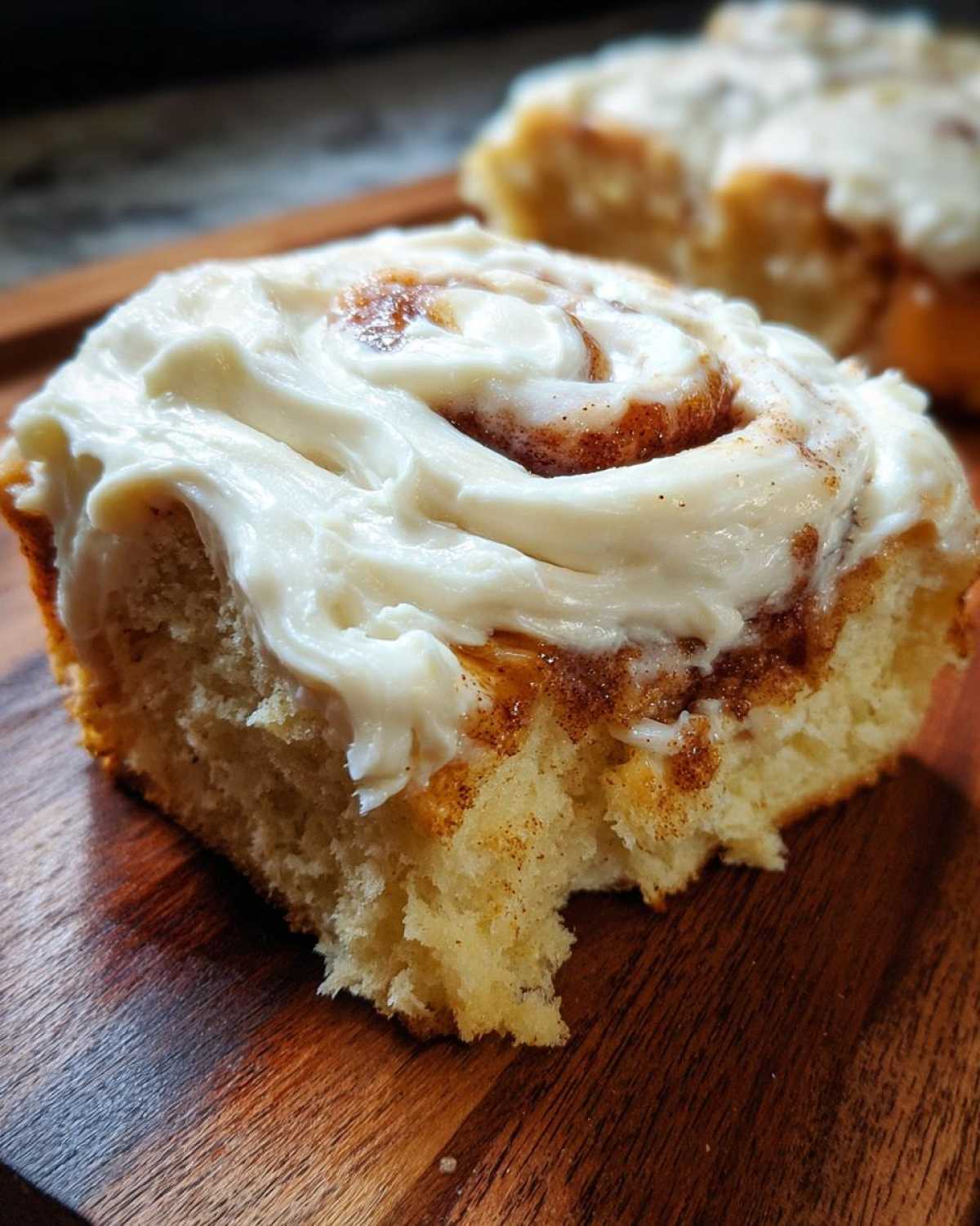 Close-up of a soft cinnamon roll generously topped with thick, white cream cheese frosting.